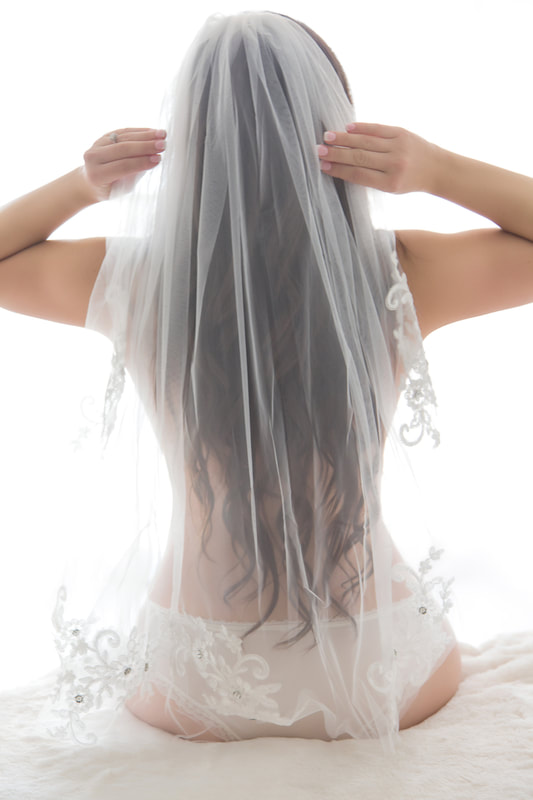 Bridal boudoir photo of a bride-to-be in her panties putting on her veil 