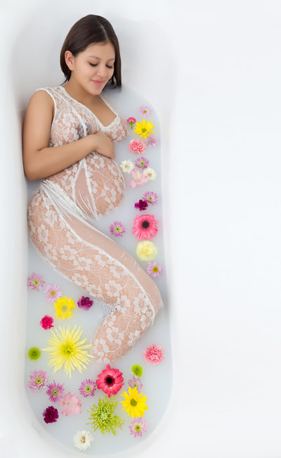 A beautiful young pregnant woman posing in a bath tub with milk bath and flowers