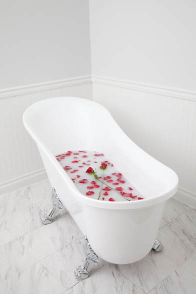 A romantic claw foot bathtub filled with milk bath and rose petals
