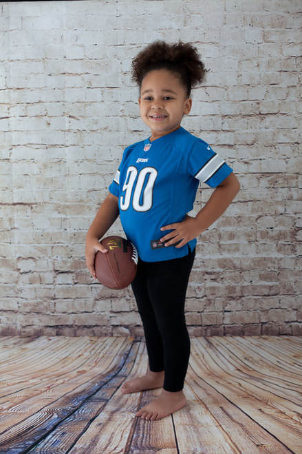 Young girl holding a football wearing a Detroit Lions football jersey