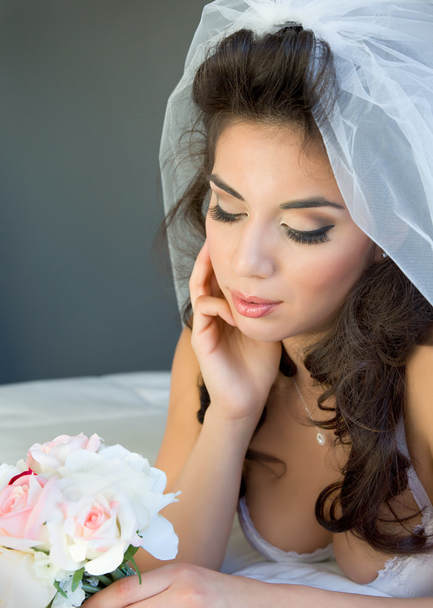 Beautiful bridal boudoir portrait of a young bride looking at her bouquet of flowers