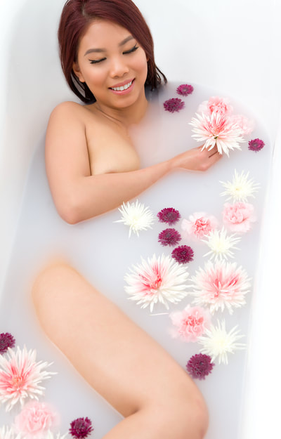 Nude milk bath boudoir photo of a naked woman holding a flower