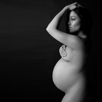 Pregnant nude woman posing with her hand covering her breasts during a nude maternity photo shoot
