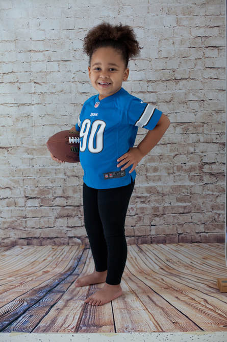Girl holding a football wearing a Detroit Lions jersey