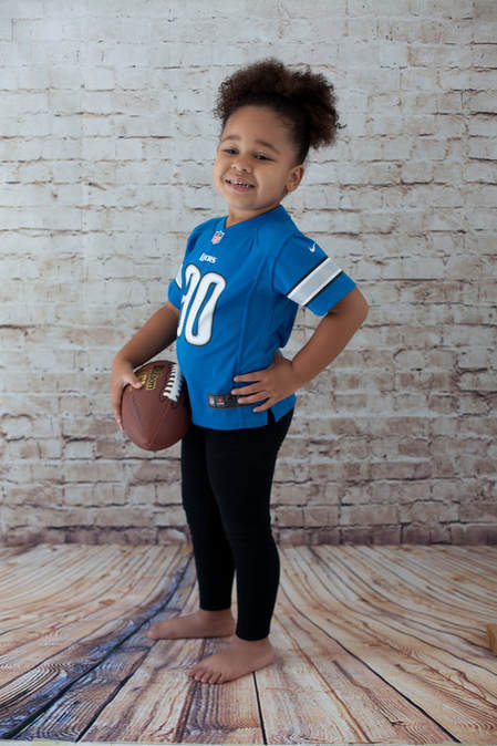 Young girl holding a football wearing a Detroit Lions jersey