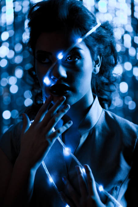 Glamour fashion photo of a young female posing with blue LED lights against her face