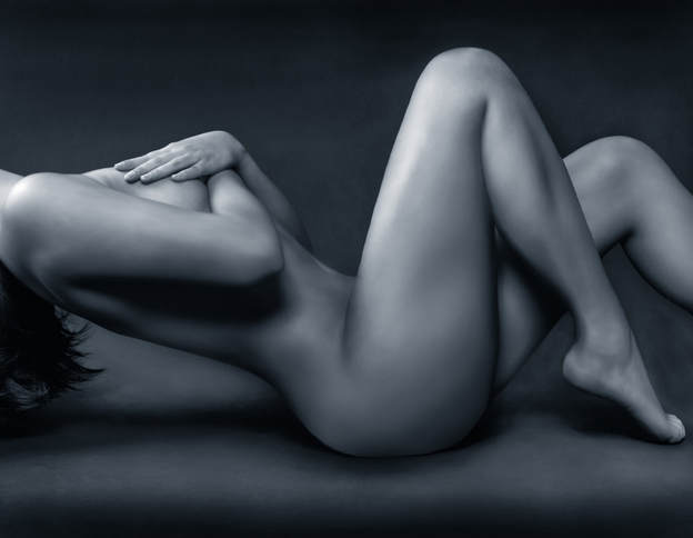 Nude Female Model Poses Laying Down With Hands Covering her bare Breasts