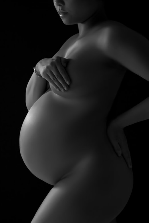 Maternity photo of a nude pregnant woman covering her breast with her hand 