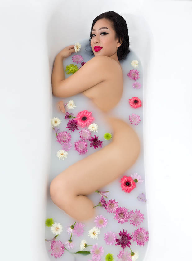 Sexy milk bath boudoir photo of a nude woman in a bath tub surrounded by milk bath and flowers.